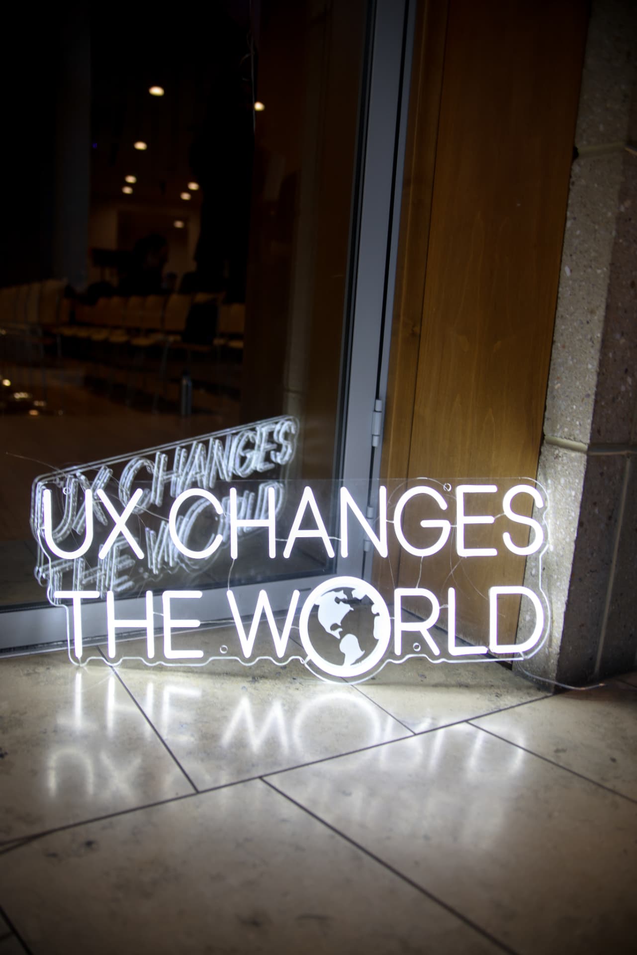 A glowing neon sign reading “UX Changes the World” at the conference entrance